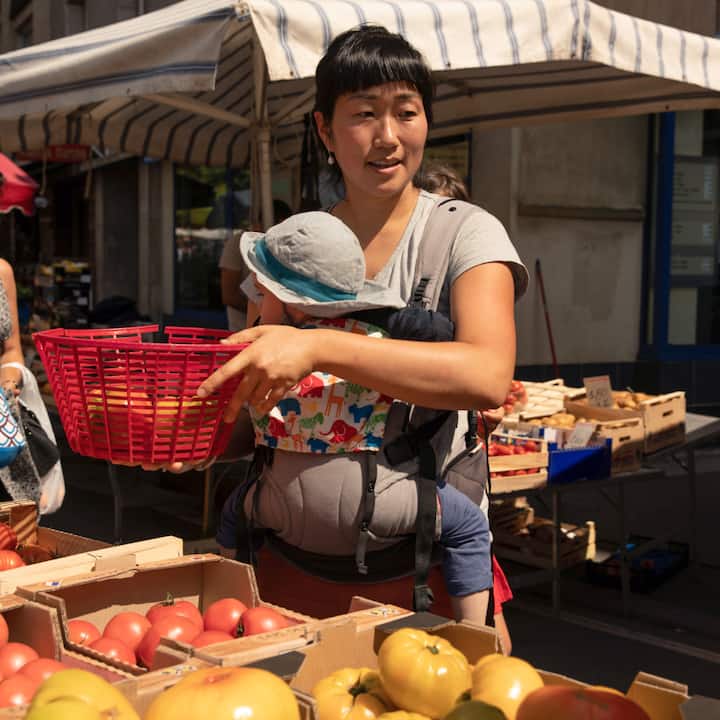 A mom wears her infant on her chest while perusing a farmers’ market. 