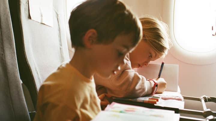 Two toddlers enjoy their coloring books while on a plane. 