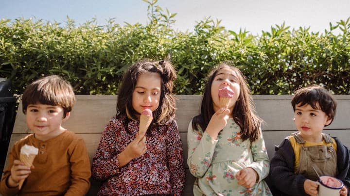 Four children sitting on a bench eating ice cream. 