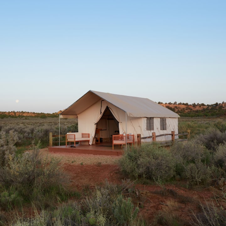 A large, welcoming tent sits in the desert at moonrise.