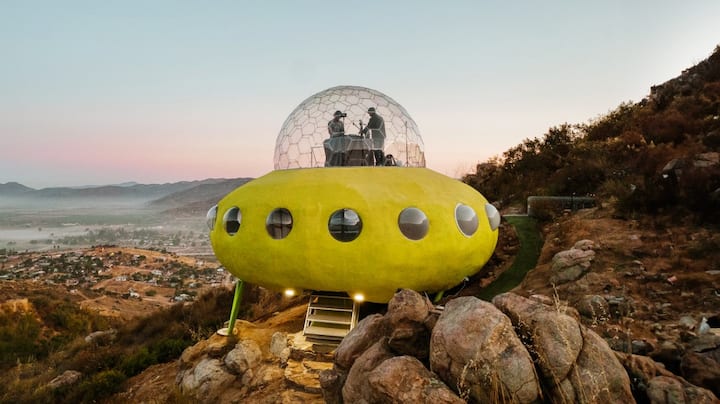 A home designed to look like a yellow UFO sits on the side of a mountain.