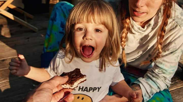 A toddler opens wide for an ice cream sandwich.