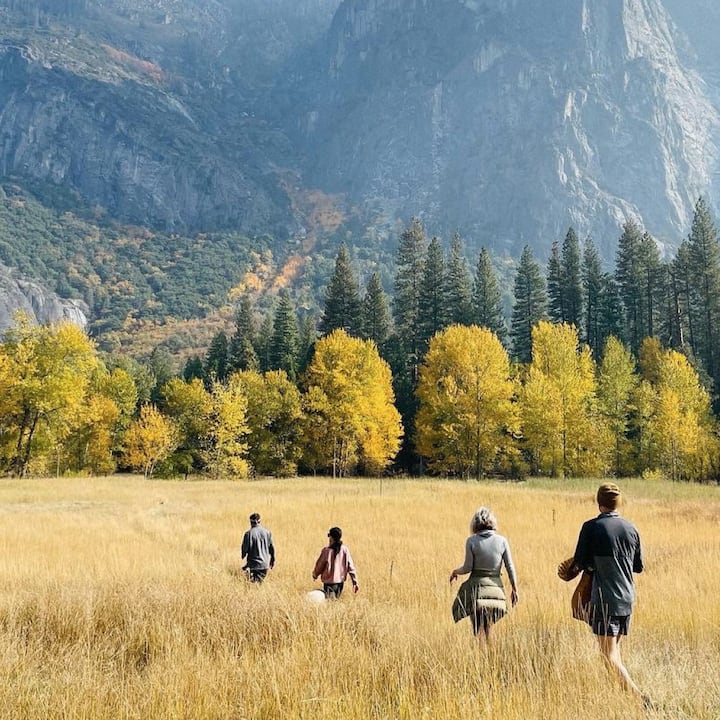 Four adults hike through scenic wheat fields surrounded by fall colors. 