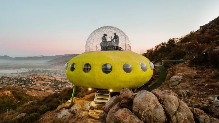 A home designed to look like a yellow UFO sits on the side of a mountain.