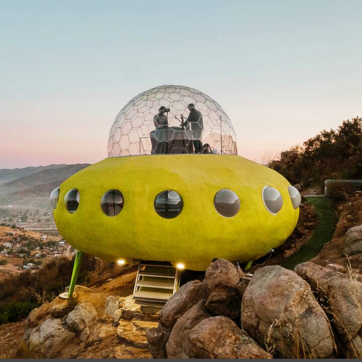 A home designed to look like a yellow UFO sits on the side of a mountain.