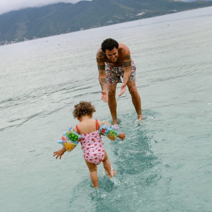 An infant, her older sister, and their dad play in shallow beach waters.
