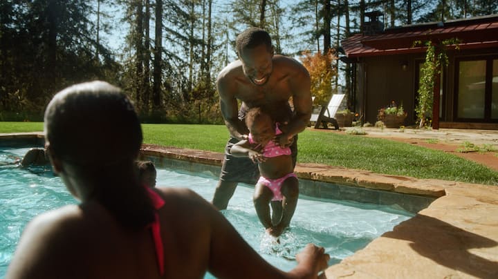 A young girl is carefully introduced to the water by her dad.