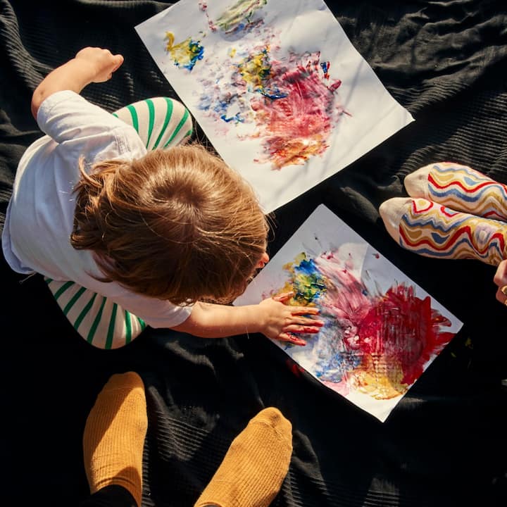 Top-down view of a toddler finger painting at the feet of her parents. 