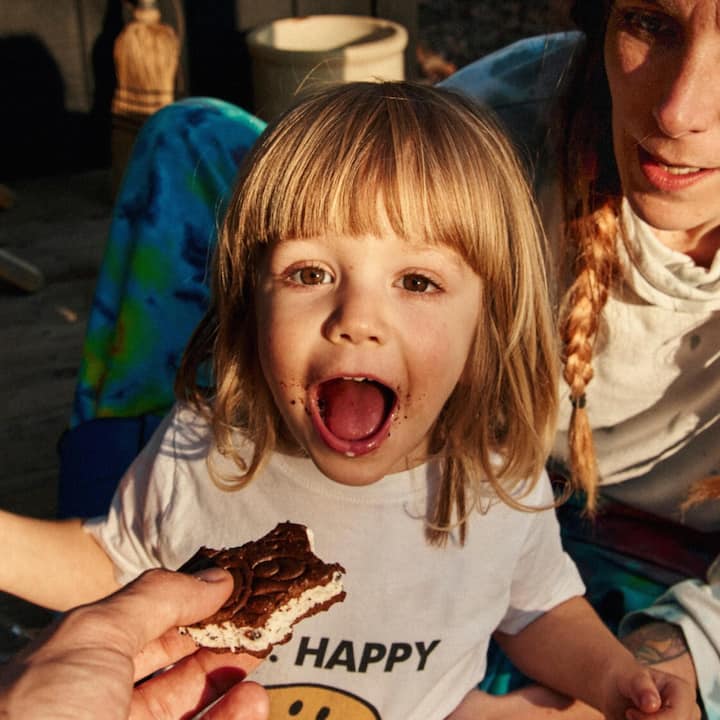 A toddler opens wide for an ice cream sandwich.