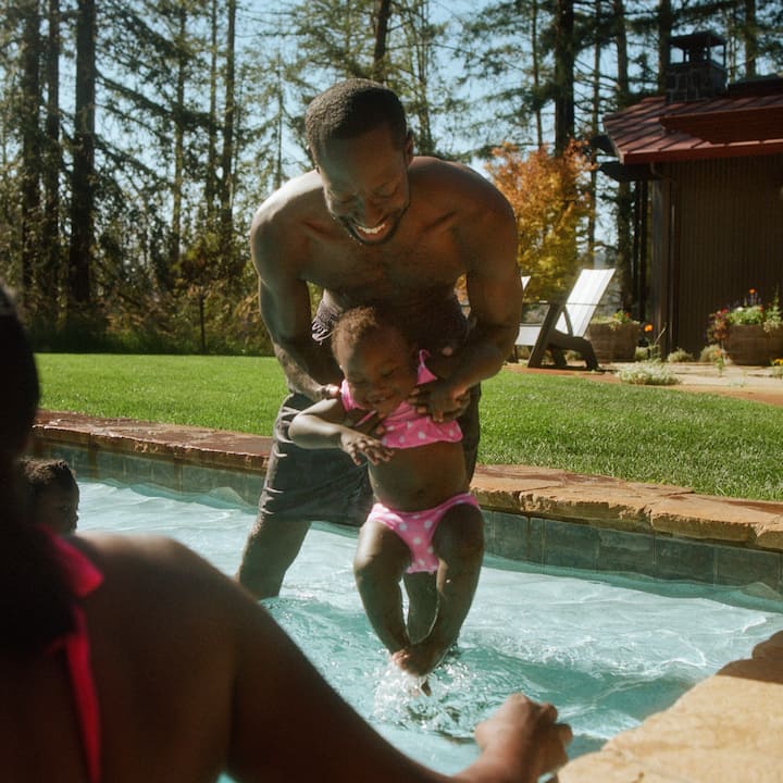 A young girl is carefully introduced to the water by her dad.