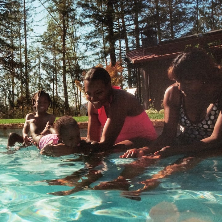 A family plays in a pool surrounded by pine trees. 