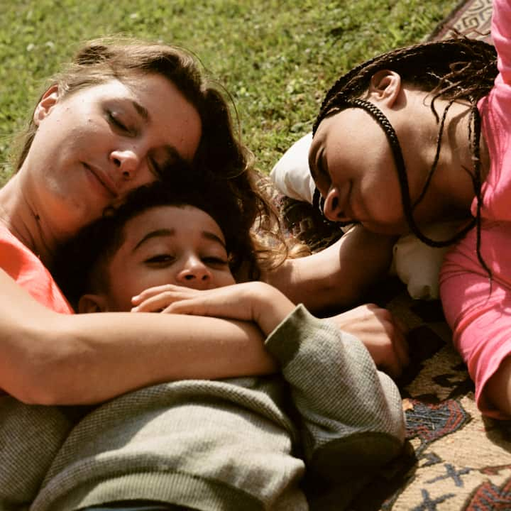 A young family naps peacefully on a picnic blanket. 