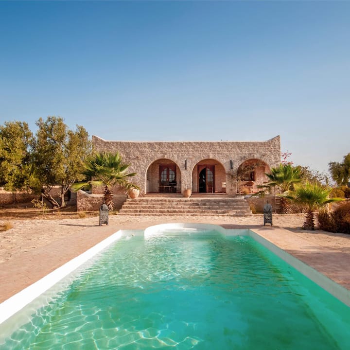 A turquoise pool sits in front of a stunning Moroccan villa.
