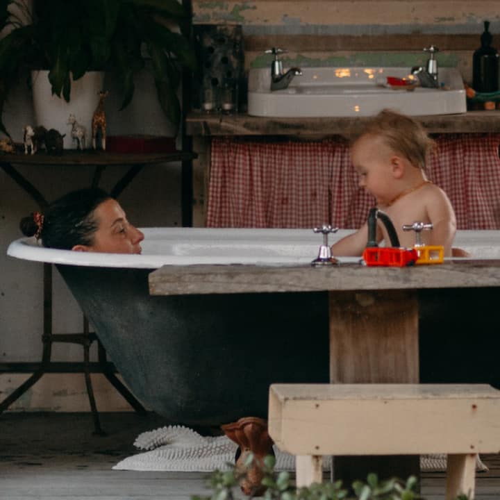 A baby takes a bath with mom in a clawfoot tub.