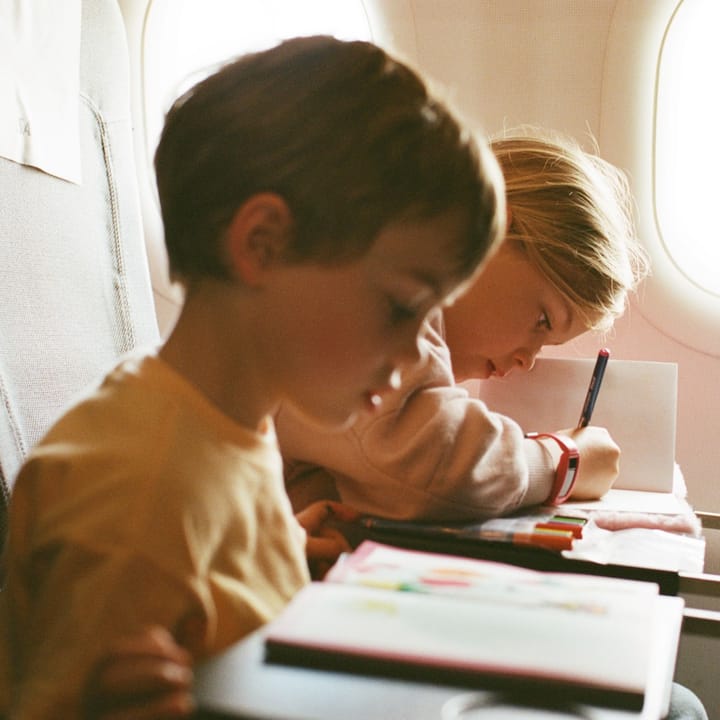 Two toddlers enjoy their coloring books while on a plane.