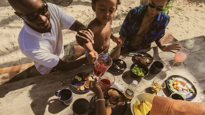 Top-down view of a young family enjoying a meal at a beachy picnic table. 