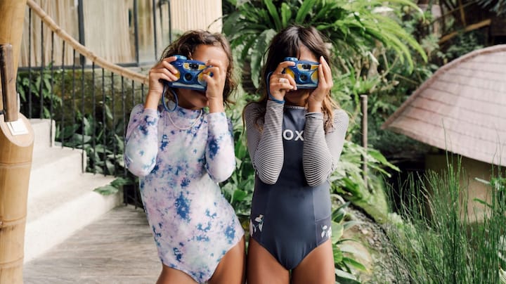 Two young girls with disposable cameras pretend to take pictures.