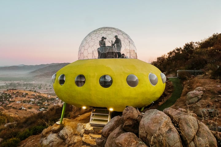 A home designed to look like a yellow UFO sits on the side of a mountain.