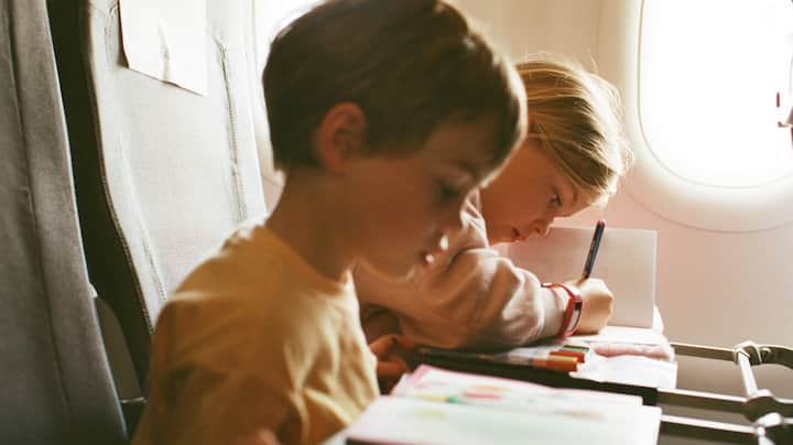 Two toddlers enjoy their coloring books while on a plane. 