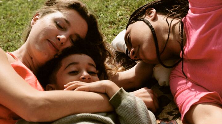 A young family naps peacefully on a picnic blanket. 