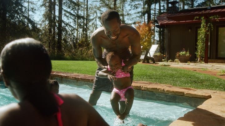 A young girl is carefully introduced to the water by her dad.