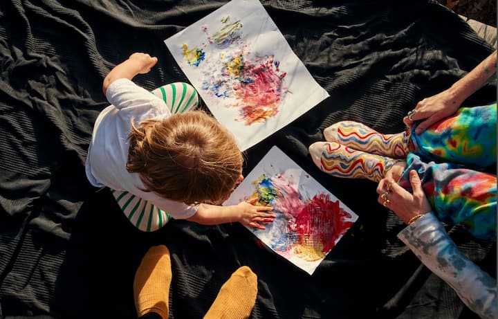 Top-down view of a toddler finger painting at the feet of her parents. 