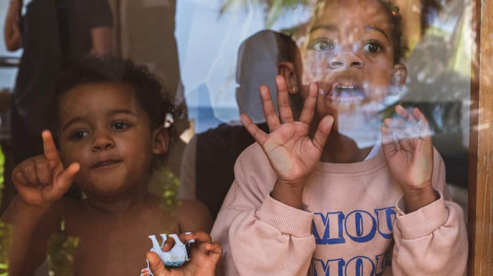 Two young kids press their faces against the glass to get their parents’ attention.