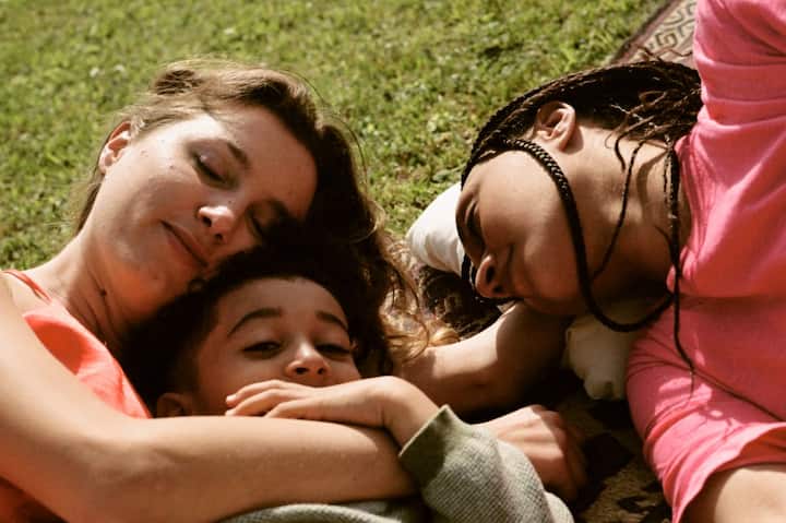 A young family naps peacefully on a picnic blanket. 