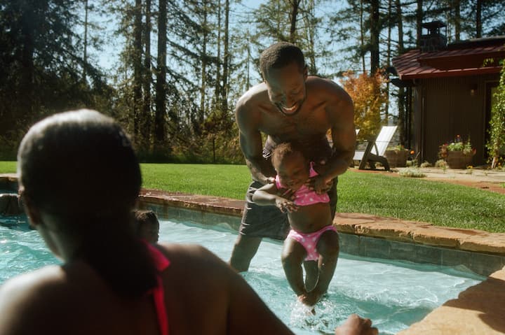 A young girl is carefully introduced to the water by her dad. 