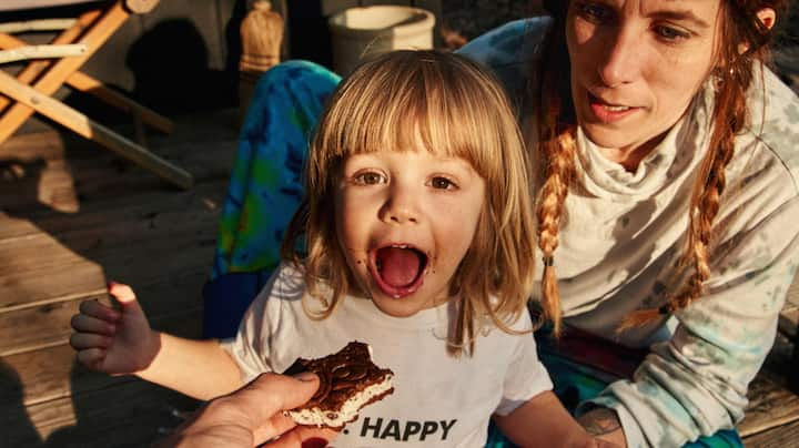 A toddler opens wide for an ice cream sandwich. 