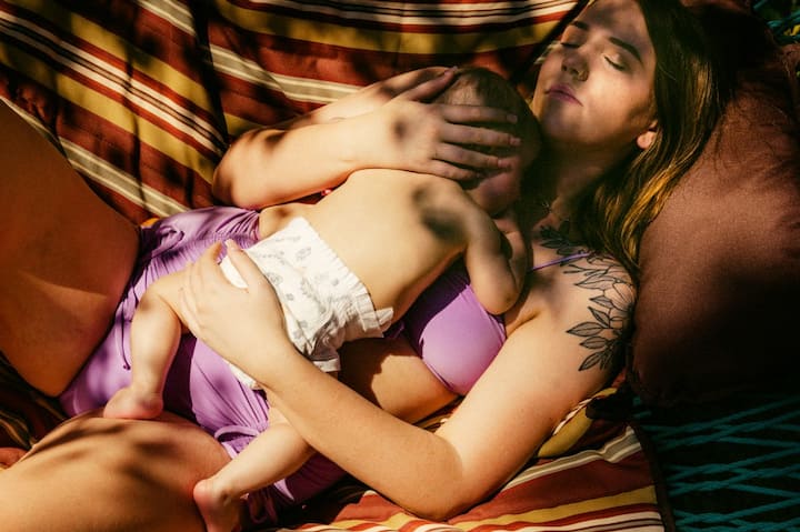A baby sleeps soundly on the chest of a woman in a hammock. 
