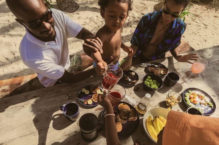 Top-down view of a young family enjoying a meal at a beachy picnic table. 