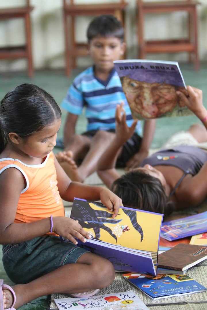 Tre bambini leggono dei libri accomodati sul pavimento.