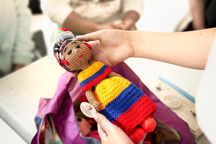 A person holds up a handcrafted doll that is dressed in yellow, blue, and red stripes.