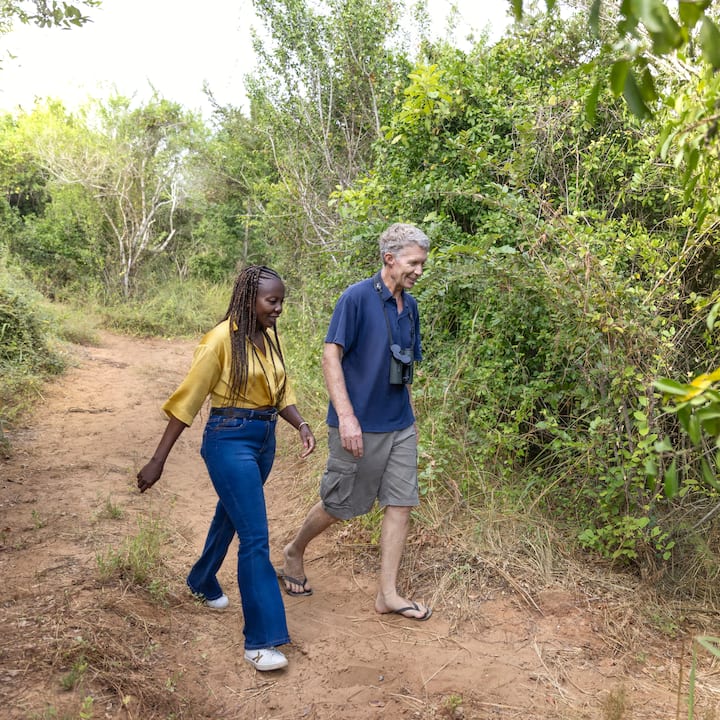 Two people walk on a dirt path in a natural area.
