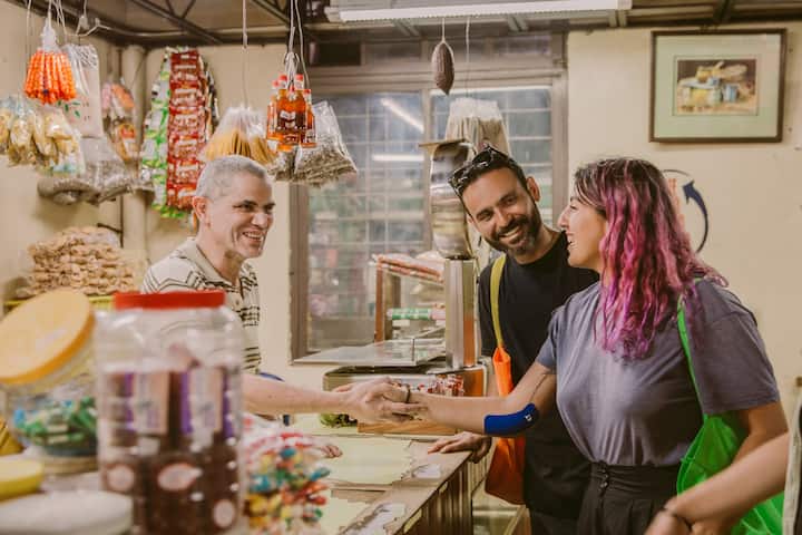 Three people smile and talk around a countertop in a colorful and brightly lit shop.