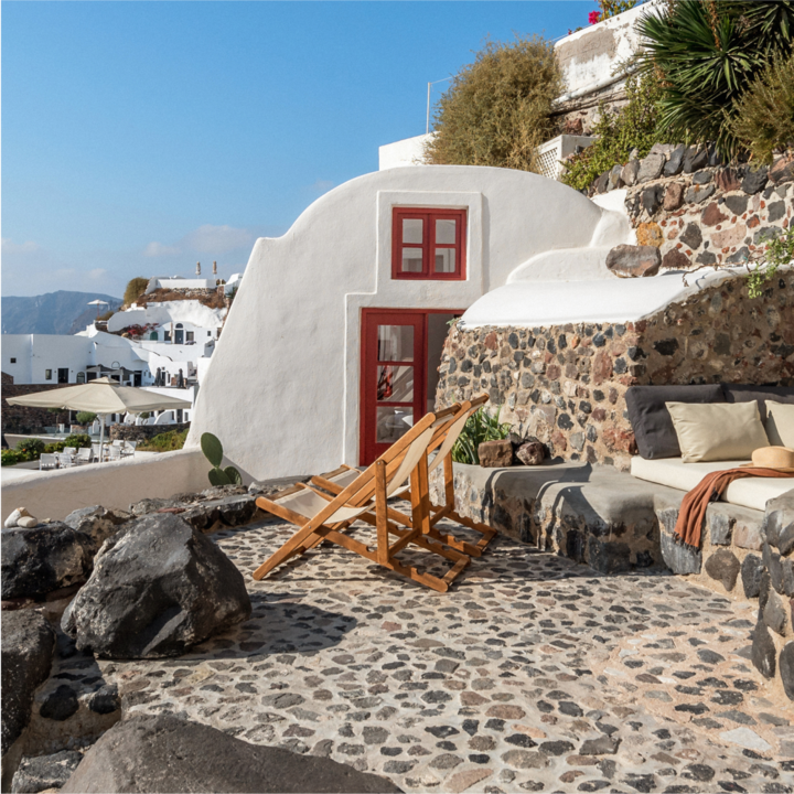 An image of an Airbnb home in an iconic European city. The image is of a beachfront home on the coast of Europe. The white-washed exterior of the home overlooks the beautiful, blue waters below. From the terrace of the home, a sunlounger sits in front of an ocean view stretching for miles.