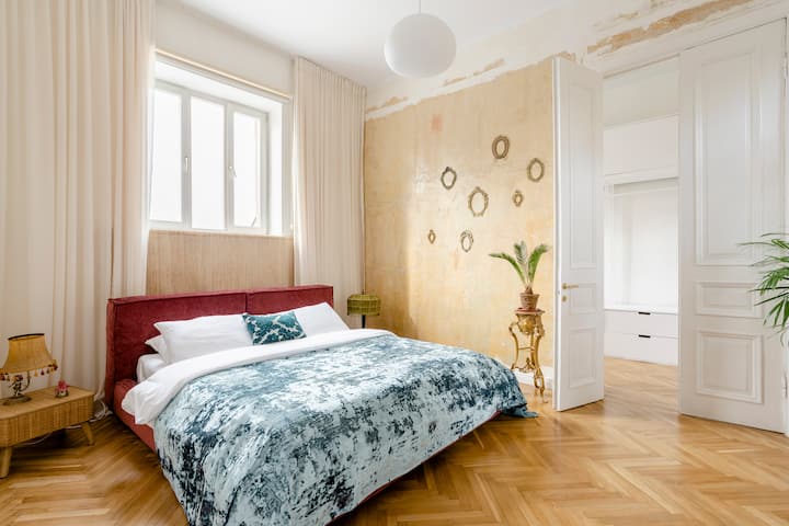 Image of a tuscan style bedroom with warm ochre walls, chevron wood floors, and white curtains.