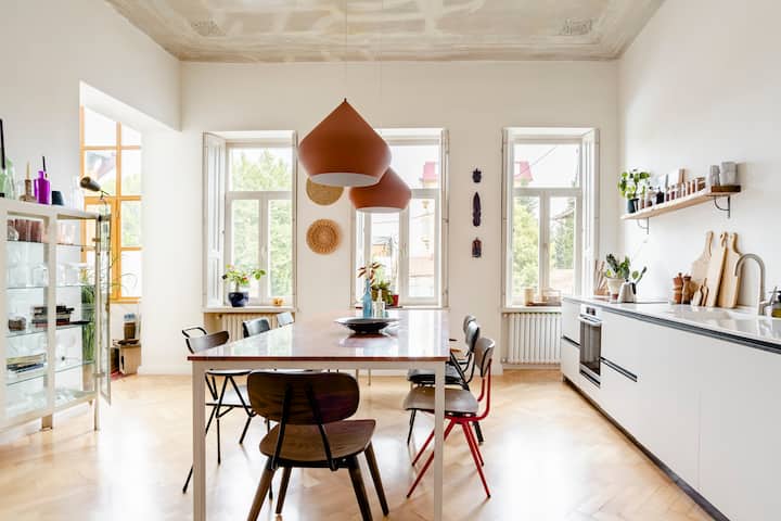 一张厨房的广角照：右侧是厨房岛，中间是餐桌，左侧是摆满餐具的餐柜。
