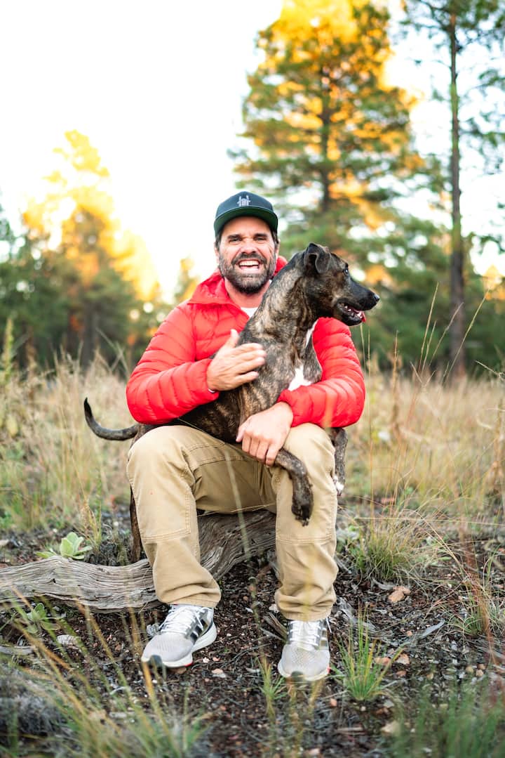 Photo of John, an experienced Co-Host based in Scottsdale, Arizona sat with his dog in a forest, laughing.