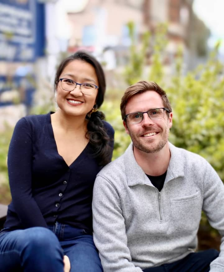 Photo of Matthew & Tiffany, sat outside of a home, both looking and smiling at the camera.