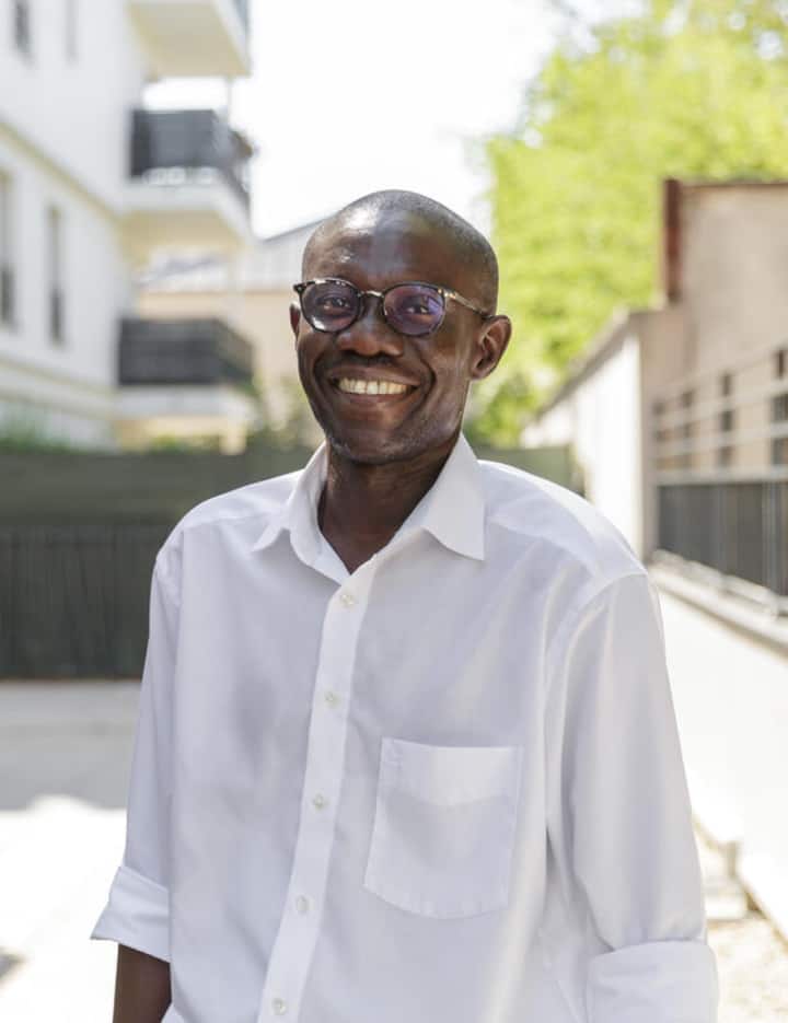 Photo of Ousmane, experienced Co-Host standing in a sunny outdoor in Nanterre, France and smiling at the camera.