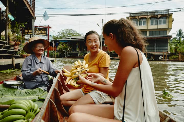 Canal inThailand, two women tourists buy bananas from female seller
