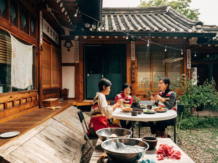 Three women share food outside a traditional home in Korea