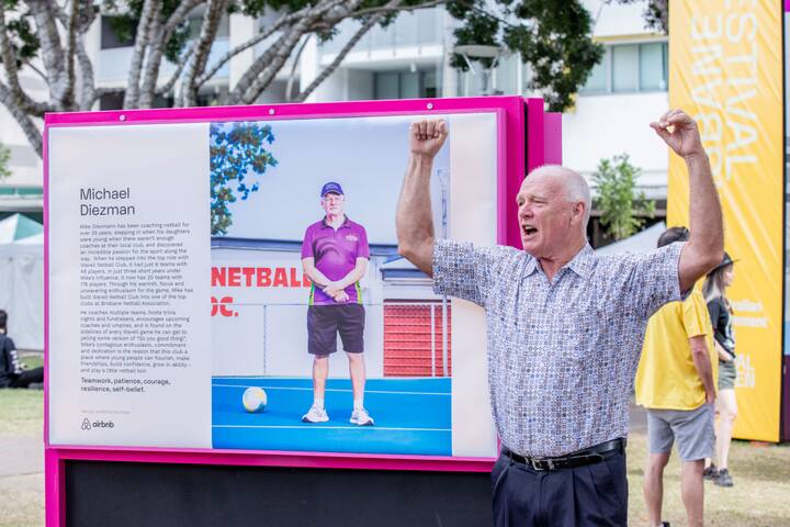 A man celebrates in front of a portrait of himself as part of the Airbnb Community Heroes program in Brisbane, Australia