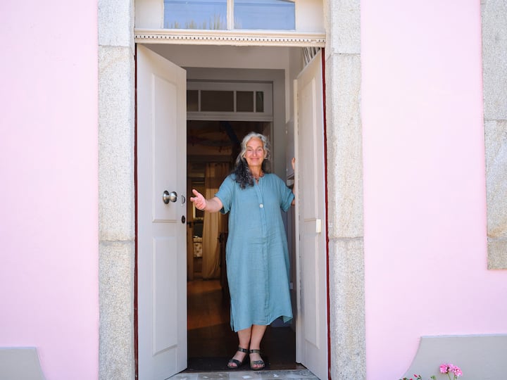 Una anfitriona en Airbnb da la bienvenida a sus huéspedes en Oporto. Con una sonrisa amable, abre la puerta de una casa acogedora con la fachada rosa.