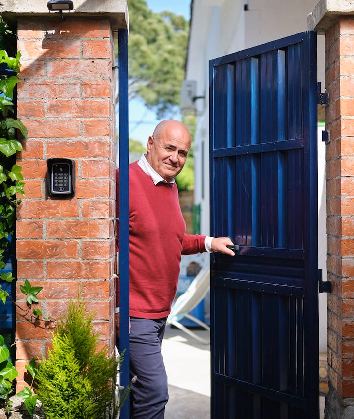 Un anfitrión en Airbnb da la bienvenida a los huéspedes en su propiedad vestido con ropa elegante. Abre la puerta de su alojamiento, bañado por el sol, con un gesto amable.