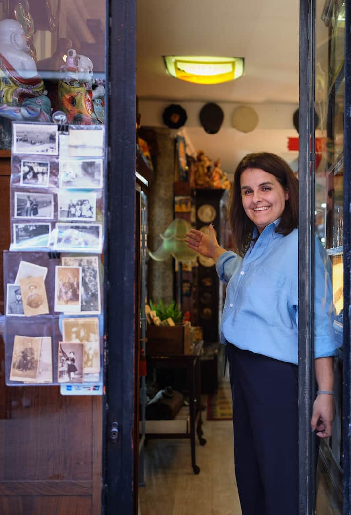 Una mujer sonríe mientras abre la puerta de su tienda de antigüedades.