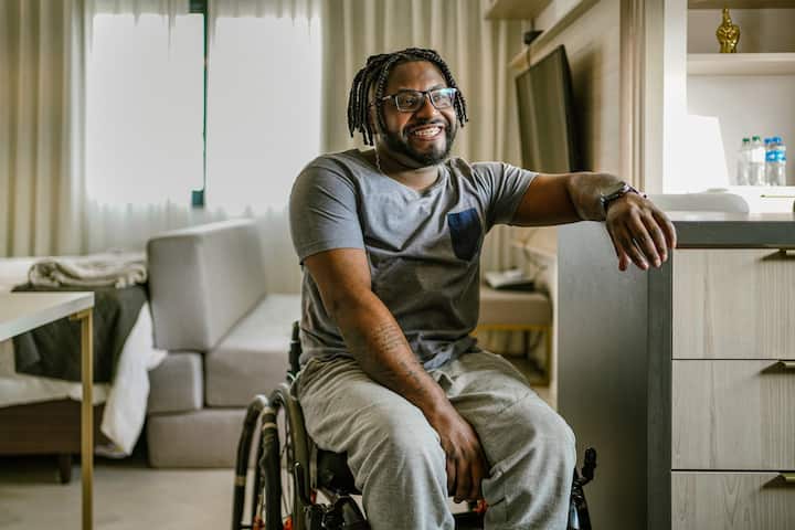眼鏡をかけたヴァンデルソン・チャベスが車椅子に座り、微笑んでいます。アパートのカウンターに腕を置いています。