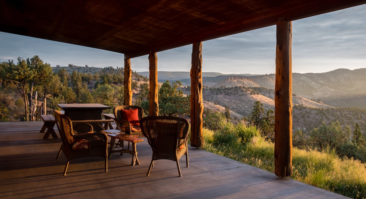 A home built from natural timbers with a panoramic view of a sunset mountain range.